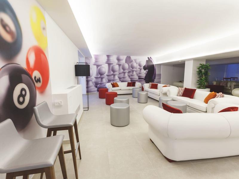Zona lounge moderna con divani bianchi, sgabelli da bar e arte decorativa murale in un hotel.
