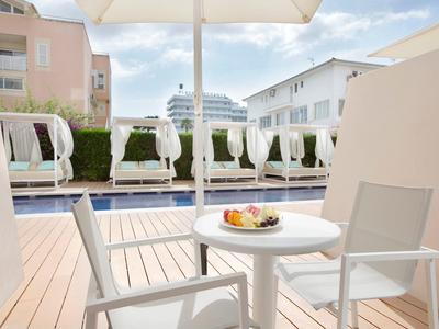 Terrace with table and chairs by a hotel pool, loungers and umbrellas in the background.