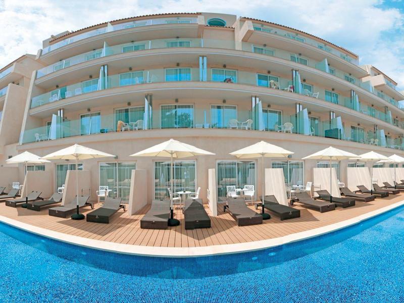 Luxury hotel with outdoor pool, sun loungers, and umbrellas under a blue sky.