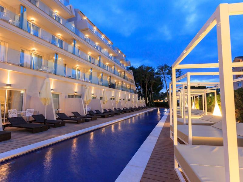 Modern hotel outdoor pool lit at dusk with lounge chairs.
