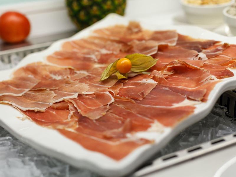 Thinly sliced ham artfully arranged on a white plate with vegetables.