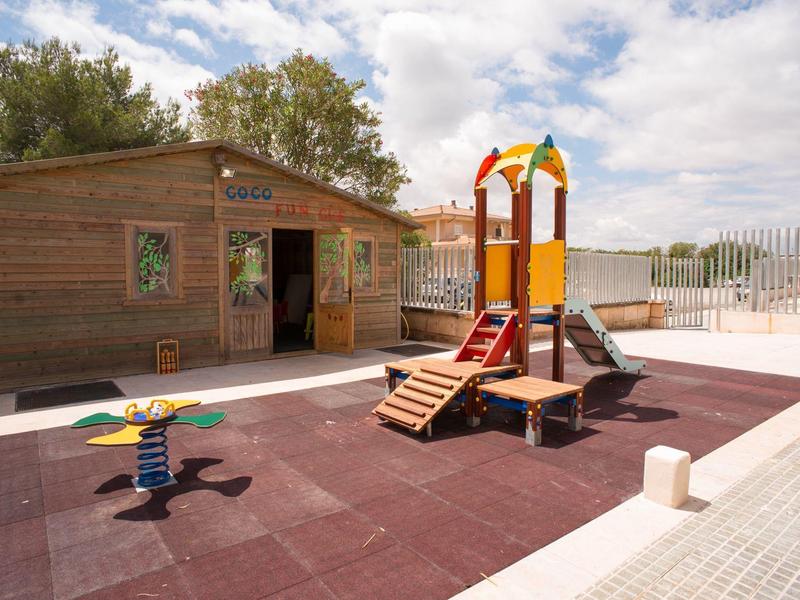 Children's playground with wooden house, slide, and spring rocker on hotel terrace in daylight.