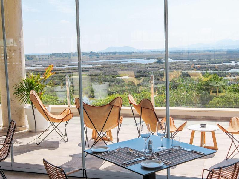 Modern dining area with large windows overlooking landscape and sea.