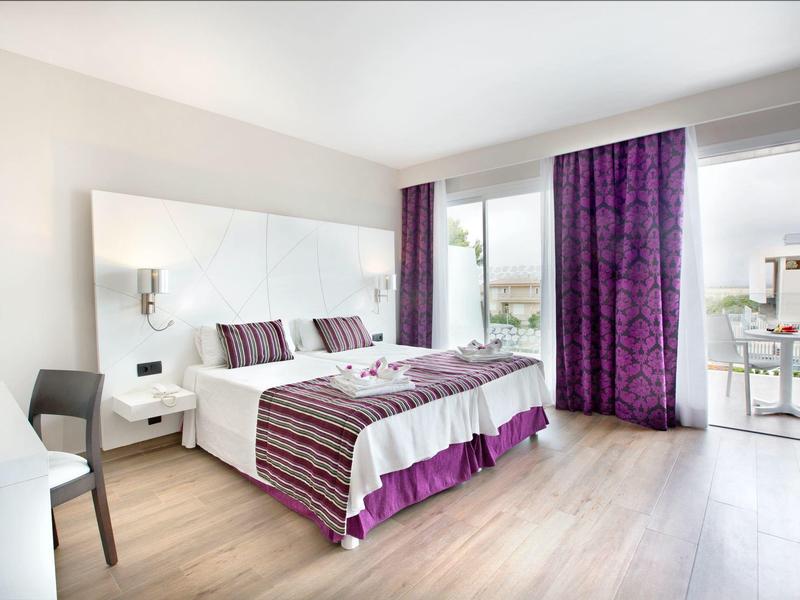 Bright hotel room with large bed, purple striped bedding, wood floor, and balcony access.