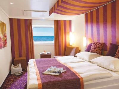 Habitación de hotel moderna con cama doble, rayas coloridas en pared y techo, vista al mar.