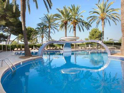 Piscina redonda de hotel con palmeras y cielo azul de fondo.