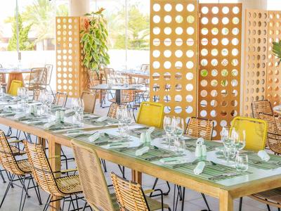 Una mesa larga elegantemente puesta en un restaurante moderno y luminoso con sillas de bambú y paredes de madera.