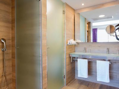 Baño moderno con revestimiento de madera, puerta de vidrio, ducha y lavabo doble.