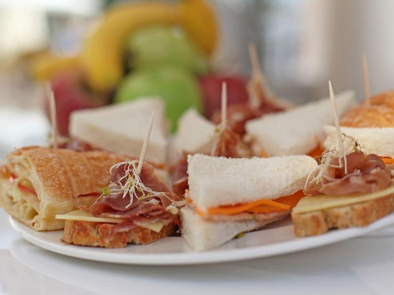 Diferentes sándwiches en un plato blanco con frutas al fondo.