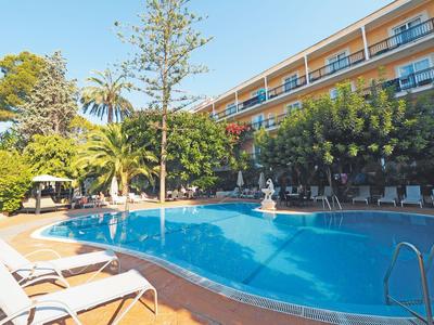Area piscina accogliente con lettini e vegetazione rigogliosa accanto a un edificio dell'hotel.