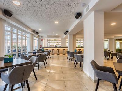 Lichte hotelbar met zitplaatsen, een bar en grote ramen.