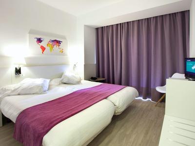 Moderne hotelkamer met twee eenpersoonsbedden, paarse gordijnen en wereldkaart aan de muur.