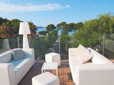 Terrasse avec canapés blancs offrant une vue sur les arbres et la mer sous un ciel dégagé.