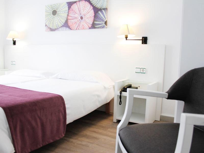 Chambre d'hôtel moderne avec lit double, literie blanche et jeté violet, chaises et œuvre murale.