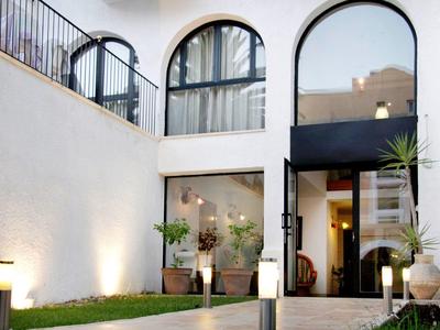 Hotel con grandi finestre ad arco e ingresso, circondato da piante e illuminazione moderna.