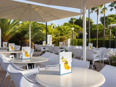 Restaurant en plein air avec tables blanches et parasols, entouré de palmiers.