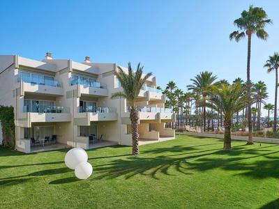 Immeuble d'appartements moderne avec balcons et palmiers sur pelouse verte sous ciel bleu.