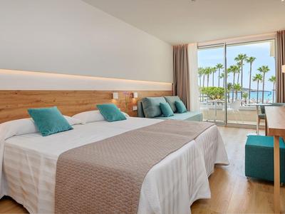 Chambre d'hôtel moderne avec deux lits, balcon et vue sur des palmiers.