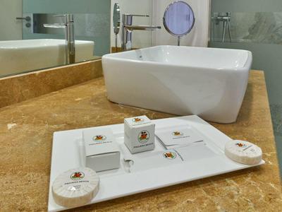 Witte hoteltoilettenartikelen op een dienblad op een bruin marmeren aanrecht naast een witte gootsteen.