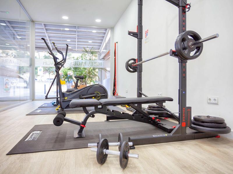 Fitnessruimte met bankdrank, halter en dumbbells op houten vloer.