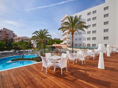 Terrasse d'hôtel avec terrasse en bois, mobilier blanc et piscine sous ciel bleu