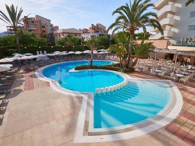 Piscina dell'hotel con palme, ombrelloni e sedie accanto a un'area ristorante.