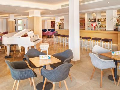 Lichte hotelbar met witte piano, houten vloer en grijze en blauwe stoelen.