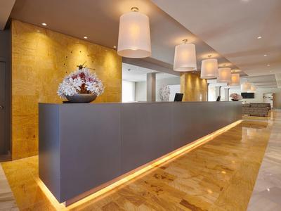 Moderner Hotel-Empfang mit langer Rezeption, goldener Wand und warmem Deckenlicht.