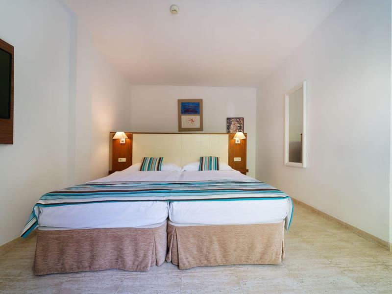 Ein schlicht eingerichtetes Hotelzimmer mit zwei Einzelbetten und weißen Wänden.