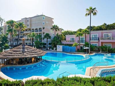 Piscina dell'hotel con ombrelloni di paglia, circondata da palme e un edificio su più piani sullo sfondo