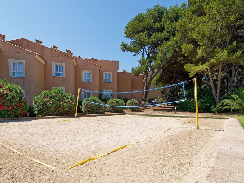 Campo da beach volley circondato da vegetazione e bungalow in fila sotto un cielo limpido