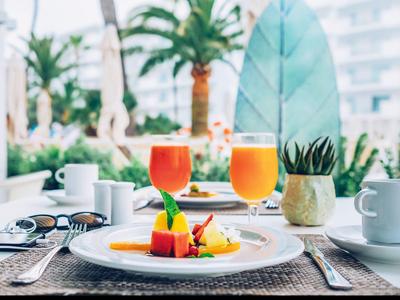 Frühstückstisch mit geschmackvoll angerichtetem Obst und zwei Gläsern Saft auf einer Terrasse.