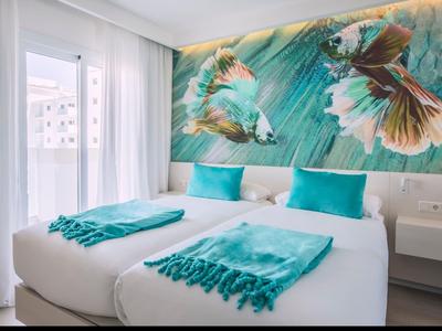 Modern hotel room with two beds, turquoise pillows and throws, bird wall art.