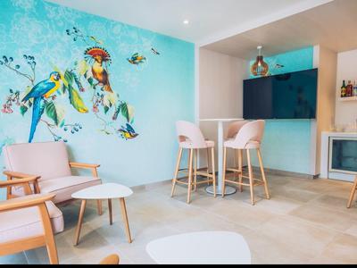 A bright lounge with wall art, armchairs, tables, and bar stools.