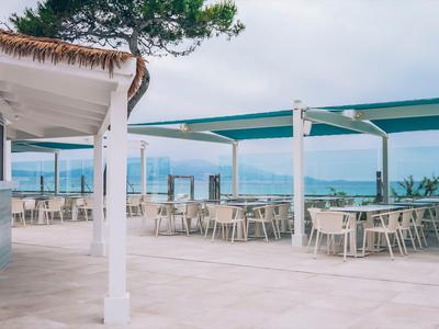 Empty outdoor dining area with white tables and chairs under blue canopies by the sea.