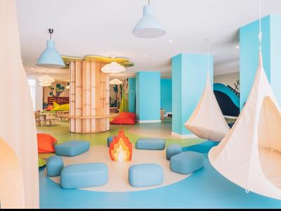 Area giochi colorata per bambini con sedi sospesi, cuscini e strutture in legno in un hotel.