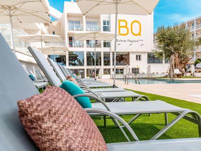 Ligstoelen met kussens onder parasols voor een hotelgebouw bij helder weer.