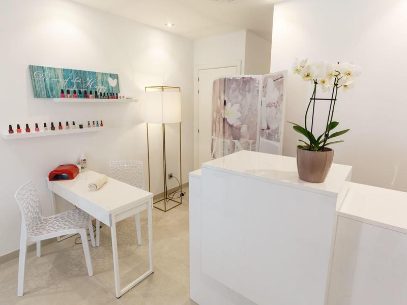 Area benessere luminosa con banco reception bianco e zona cura unghie con sedia e lampade