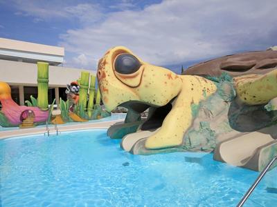 Toboggan aquatique enfant en forme de grenouille à la piscine extérieure sous un ciel bleu.