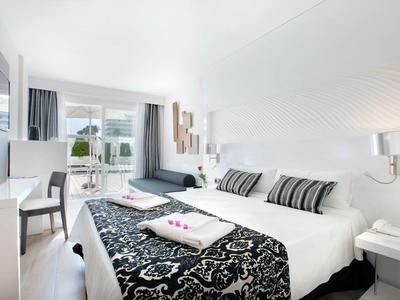 Chambre d'hôtel moderne avec grand lit, murs blancs et coussins décoratifs.