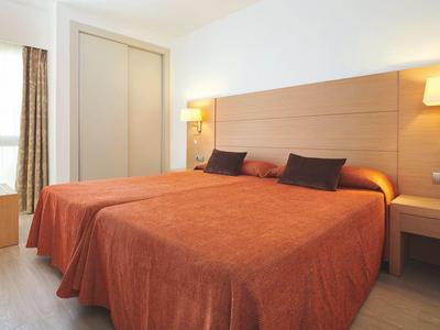 Bright hotel room with two single beds, orange bedspreads, and modern furnishings.