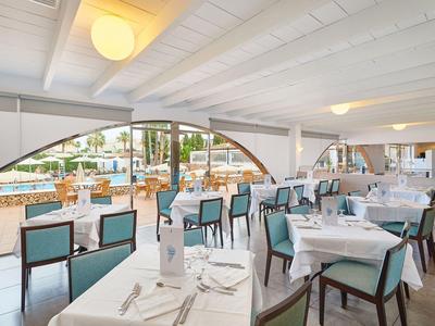 Sala da pranzo luminosa con tavoli bianchi e vista sulla piscina esterna.