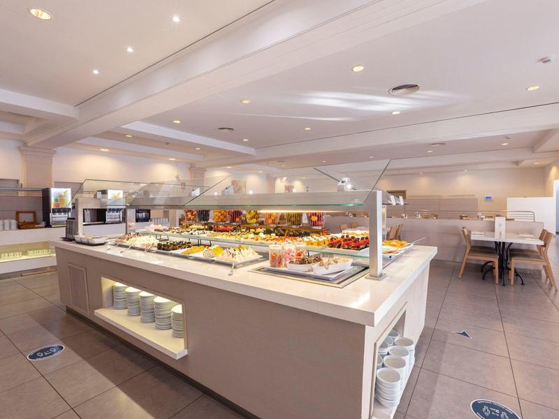 Postazione buffet in una sala da pranzo di un hotel luminosa con varie opzioni per la colazione.