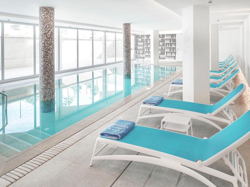 Piscina interna moderna con lettini blu e grandi finestre che lasciano entrare la luce naturale.