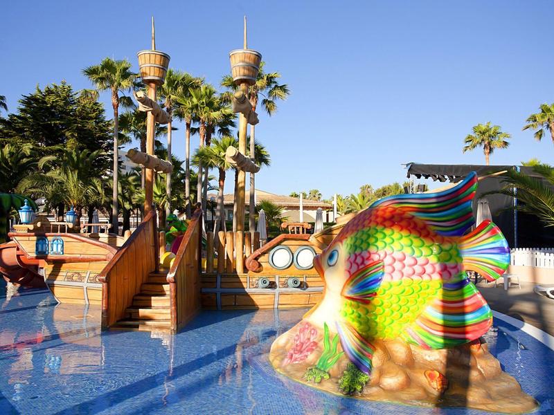 Piscina con scivoli colorati e strutture nautiche circondate da palme.