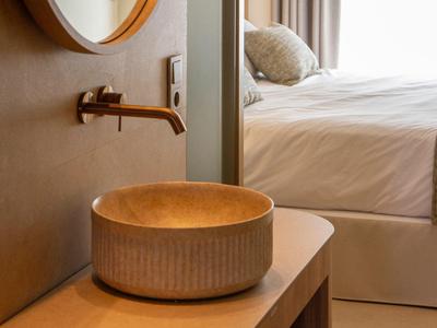 Modern round sink basin on a wooden vanity next to a bed.