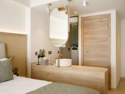 Bright bedroom with wooden dresser, round mirror, and door in natural wood.
