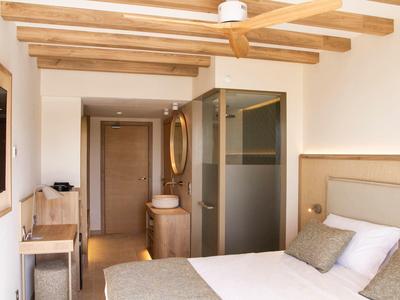 Modernes Hotelzimmer mit Holzbalken, Doppelbett, Glasdusche und schlichtem Holzmöbel.