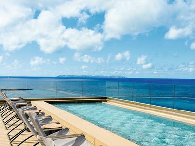 Wohnbereich mit Pool und mehreren Liegestühlen, Glasgeländer und Meerblick unter blauem Himmel.