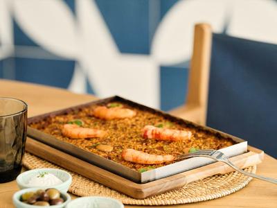 Backblech mit gebratenen Garnelen auf Holzplatte, daneben kleine Schalen mit Oliven und Saucen.